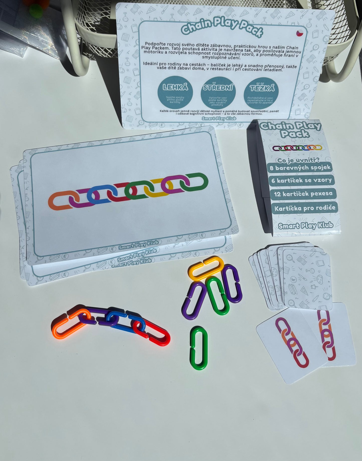 Colorful chain links and cards on a white surface with packaging in the background.